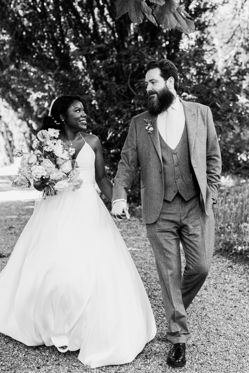 Black-and-white wedding portrait of a couple walking hand in hand outdoors